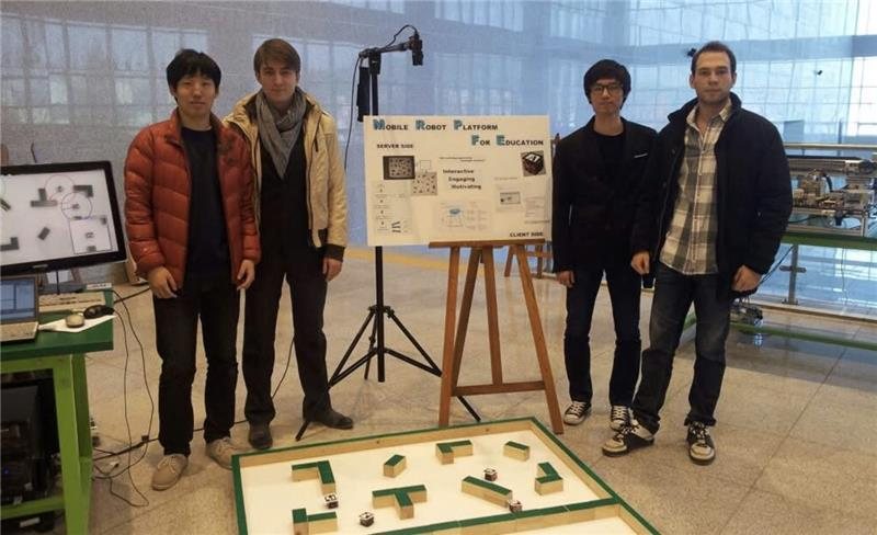 Four team members standing beside a poster for the Mobile Robot Platform for Education, with the maze arena in front of them.