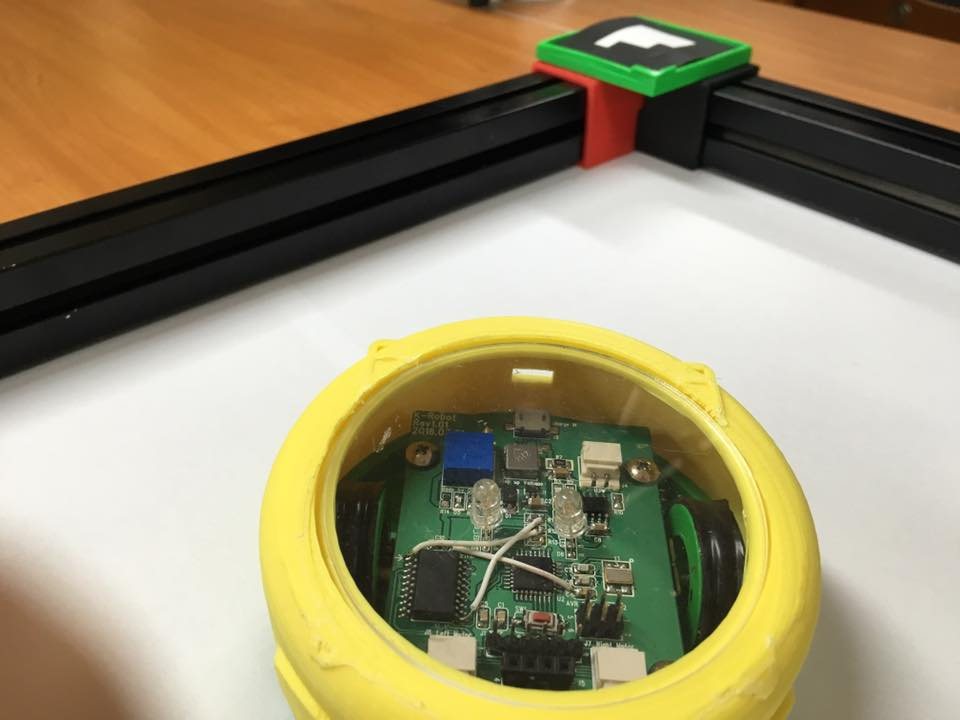 The second-generation robot opened up: a round yellow shell holding its circuit board, beside the arena's corner post.